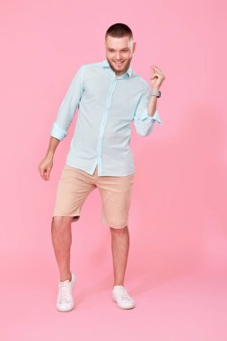 Neşeli genç adam pembe arka planda dans ediyor. Tatil yazı. Tüm vücut