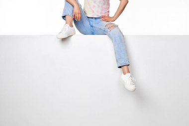 female legs in jeans and white sneakers sitting on white banner. copy space