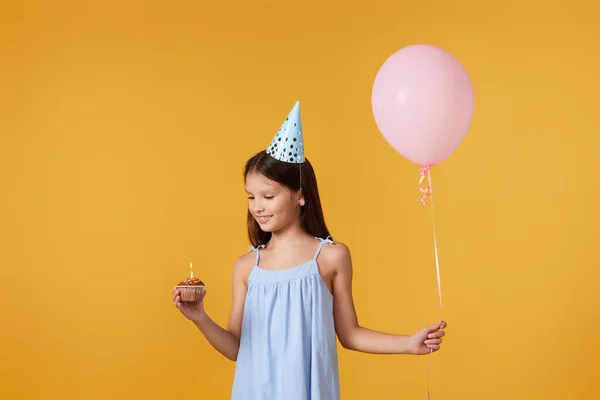 Κοριτσάκι Μπλε Κώνο Κόμμα Κρατώντας Cupcake Και Μπαλόνι Κίτρινο Φόντο — Φωτογραφία Αρχείου
