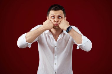 brunette man in t-shirt smiling and puffing cheeks with funny face isolated on pink background