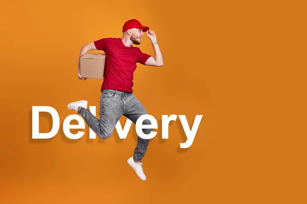 Delivery man in red cap, t-shirt holding cardboard box and jumping isolated on orange background