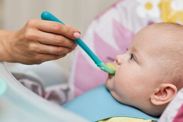 Mom feeds her baby girl with a spoon on baby chair. mother gives food to her baby