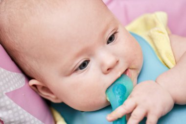 cute baby girl eating with spoon on baby chair , close-up