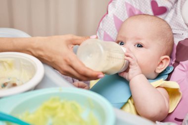 Mom feeds her adorable baby girl from a bottle with milk