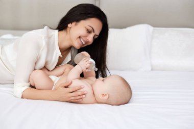 Yeni doğmuş bebeğini beyaz bir yatak odasında besleyen mutlu bir anne. Annem bir şişe mama sütü tutuyor.
