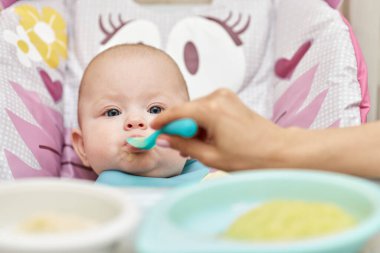 Mom feeds her baby girl with a spoon on baby chair. mother gives food to her baby