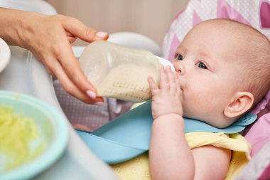 Mom feeds her adorable baby girl from a bottle with milk