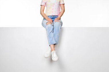 Beyaz pankartta oturan kot ve beyaz spor ayakkabılı kadın bacakları.