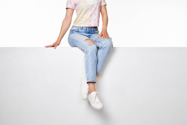 Beyaz pankartta oturan kot ve beyaz spor ayakkabılı kadın bacakları.