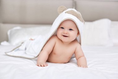 Sevimli bir kız bebek, beyaz yatakta uzanıyor. Kafasında ve vücudunda havluyla. Hijyen ve bebek bakımı kavramı.