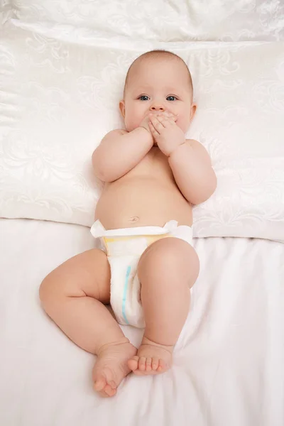 little smiling baby girl in wet diaper on bed with white linen. blue stripe on diaper moisture indicator