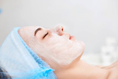 Güzellik salonunda yüzünde nemlendirici maske olan güzel bir kadın. yakın plan