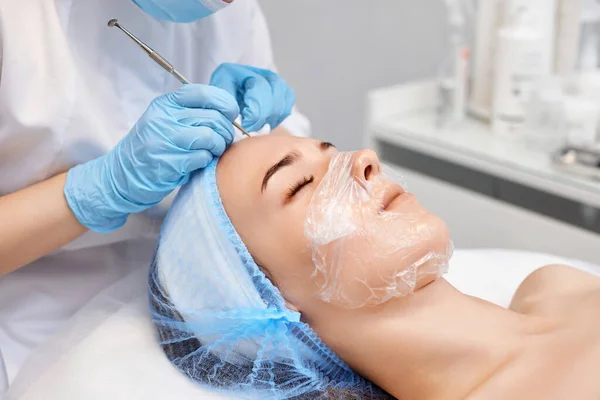 young woman during a mechanical face cleansing procedure at beauty clinic. Cosmetologist making procedure for cleaning skin with steel tool from blackheads and acne
