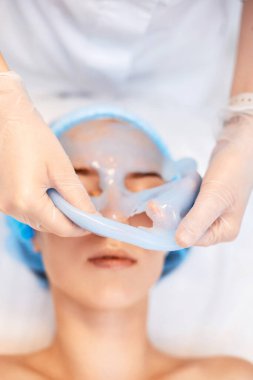 Güzellik uzmanı kaplıcadaki güzel kadının yüzündeki mavi aljinat maskesini çıkarıyor. spa tedavileri