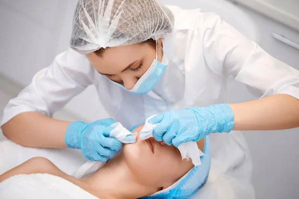 young woman during a mechanical face cleansing procedure at beauty clinic. Cosmetologist making procedure for cleaning skin with steel tool from blackheads and acne