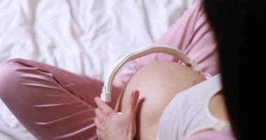 Yatak odasında karnına kulaklık takan güzel hamile bir kadın. en üstteki görünüm