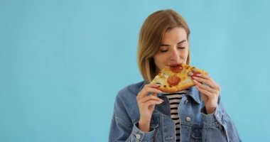 Genç bir kadın pizza yiyor ve mavi arka planda mutlu görünüyor. Boşluğu kopyala