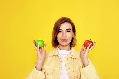 Gülümseyen sarışın kadın sarı arka planda iki elma arasında karar veriyor..