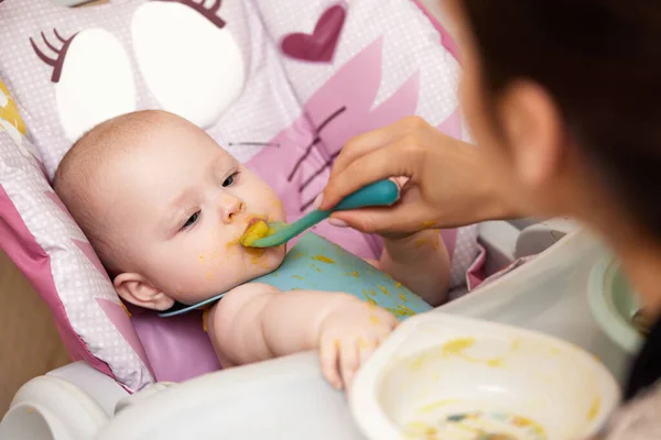 妈妈在婴儿椅上用勺子喂她的女婴 母亲给7个月大的婴儿喂食 — 图库照片
