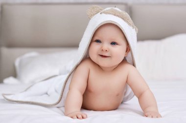 Sevimli bir kız bebek, beyaz yatakta uzanıyor. Kafasında ve vücudunda havluyla. Hijyen ve bebek bakımı kavramı.