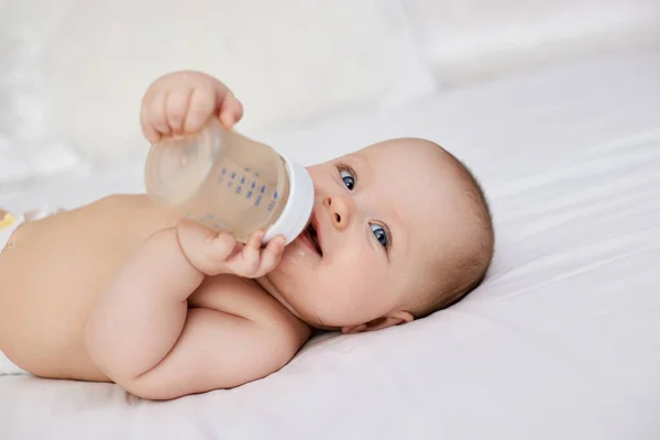 迷人的女婴躺在床上 喝着一瓶水 — 图库照片