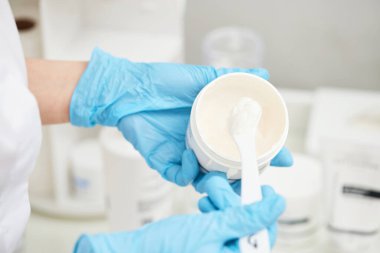 Güzellik uzmanının ellerinde lüks yüz kremi olan beyaz plastik kavanozun yakın çekimi. Cilt bakım ürünleri