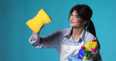Lastik eldivenli genç bir kadın ve temiz önlüklü bir kova dolusu temizlik malzemesi ve mavi arka planda sarı süngerli temizlik..