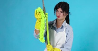 Profesyonel temizlikçi kız lastik eldivenli ve temiz önlüklü. Mavi arka plandaki plastik zemine yeşil bir bez koydu..