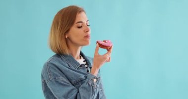 Gülümseyen güzel sarışın kadın mavi arka planda zevkli çöreklerle yemek yiyor. Boşluğu kopyala