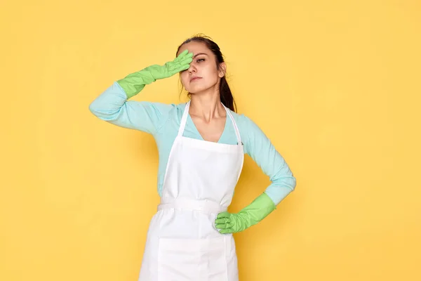 tired woman in gloves and cleaner apron on yellow background