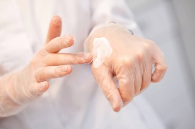 Eldivenli güzellik uzmanı eline krem sürüyor ve kremin dokusunu gösteriyor.