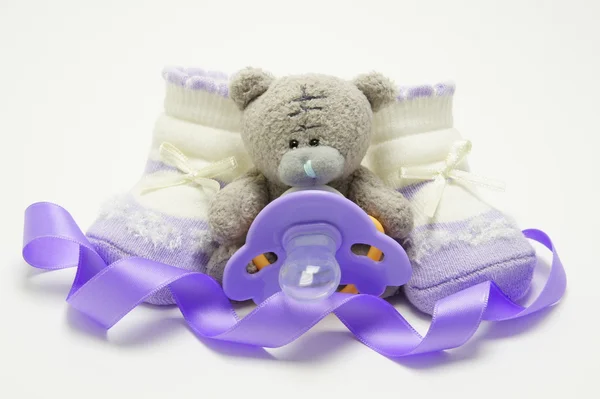 Bear with pacifier and lilac baby's bootees. — Stock Photo, Image