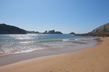 Arka planda kayalıklar olan sakin, kumlu bir sahil.