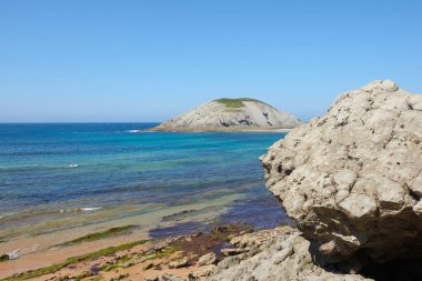 Güzel mavi gökyüzü olan sakin bir denizin yanındaki sarp kayalıklar