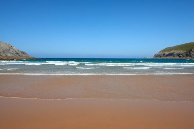 Arka planda kayalıklar olan sakin, kumlu bir sahil.