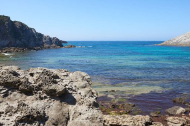 Güzel mavi gökyüzü olan sakin bir denizin yanındaki sarp kayalıklar