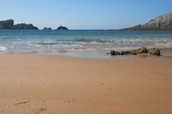 Arka planda kayalıklar olan sakin, kumlu bir sahil.