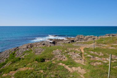 Bitkilerle çevrili vurucu uçurumlar ve turkuaz mavi bir deniz..