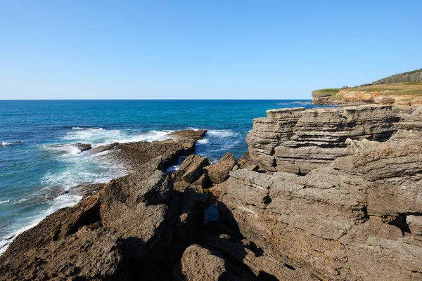 Derin mavi denizi ve berrak mavi gökyüzü olan sarp kayalıklar.