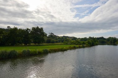 Güzel bir nehir, bulutlu bir gökyüzünün altında yemyeşil bitki örtüsüyle çevrili..