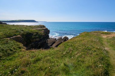 Bitkilerle çevrili vurucu uçurumlar ve turkuaz mavi bir deniz..