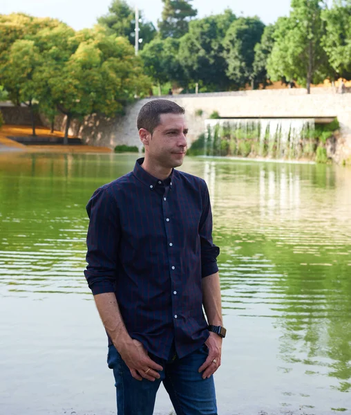 A young man in jeans posing at ease in a park.