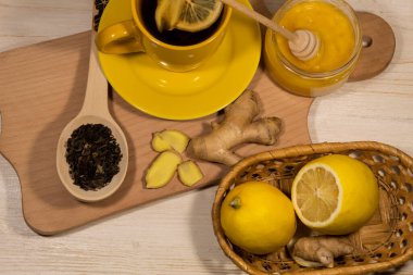 Masada limon ve zencefilli bir fincan çay var. Yakınlarda bir kavanoz bal, demlemek için bir kaşık çay, limon ve zencefil var..