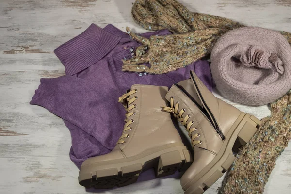 Kalın giysiler arka planda yatar. Süveter, atkı, bere ve deri ayakkabılar..