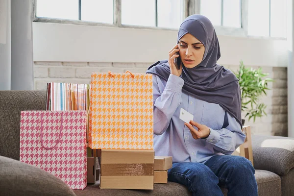Grave donna musulmana in possesso di una carta di credito e parlare al telefono — Foto Stock