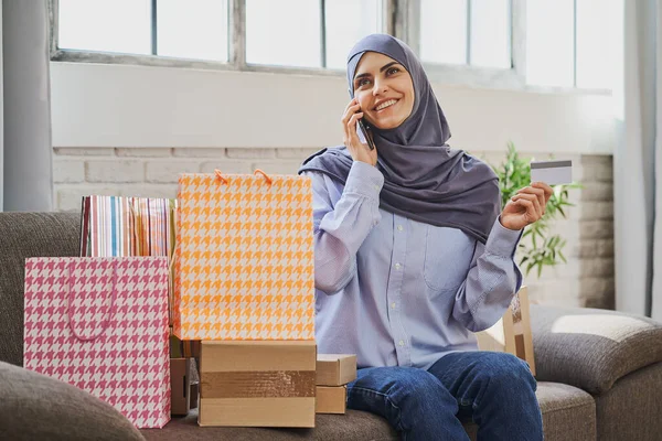 Dreaming Arabian girl holding a credit card and talking on the phone — Stock Photo, Image