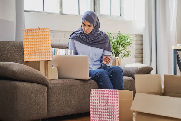 Genç Müslüman kadın bir internet dükkanından hediye alıyor ve kredi kartı kullanıyor. Stok Fotoğraf