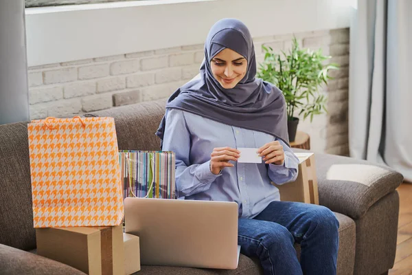 Wanita muslim cantik duduk di sofa dan membeli sesuatu secara online Stok Gambar Bebas Royalti