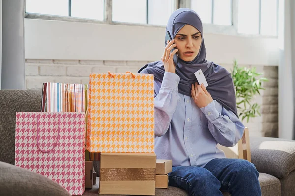 Upset Arabian woman holding a credit card and talking on the phone Stock Photo