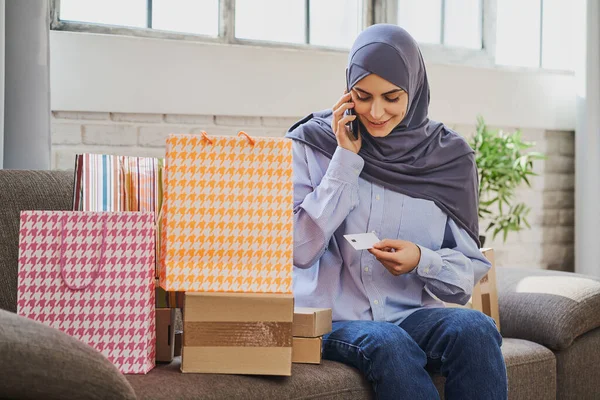 嬉しいイスラム教徒の女性が電話で話してプラスチックカードを持ってる ロイヤリティフリーのストック画像
